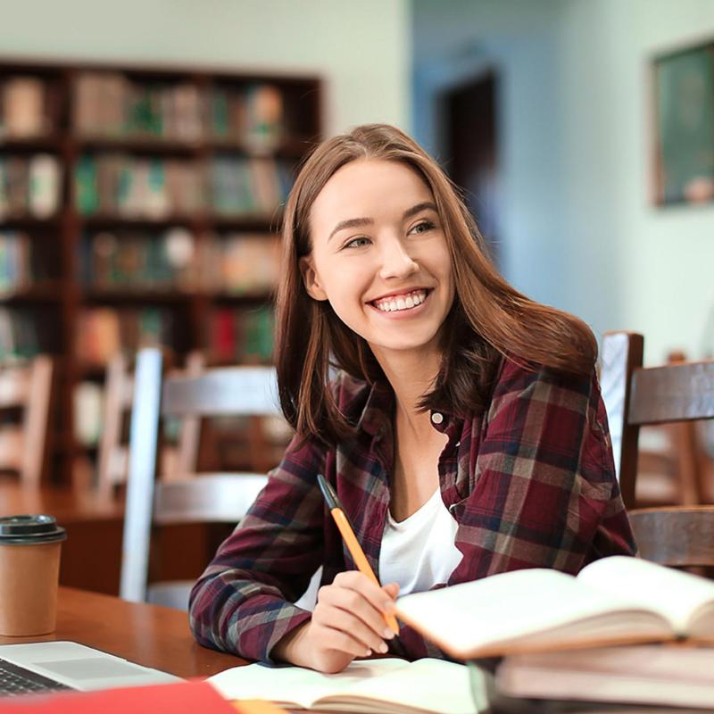 a student with a pen in hand and papers and books in a library.