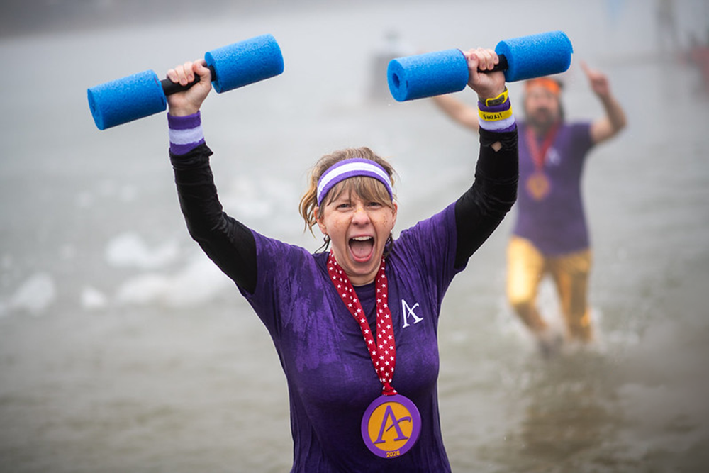 A woman smiling, wearing purple shirt holding pool noodle weights in the air