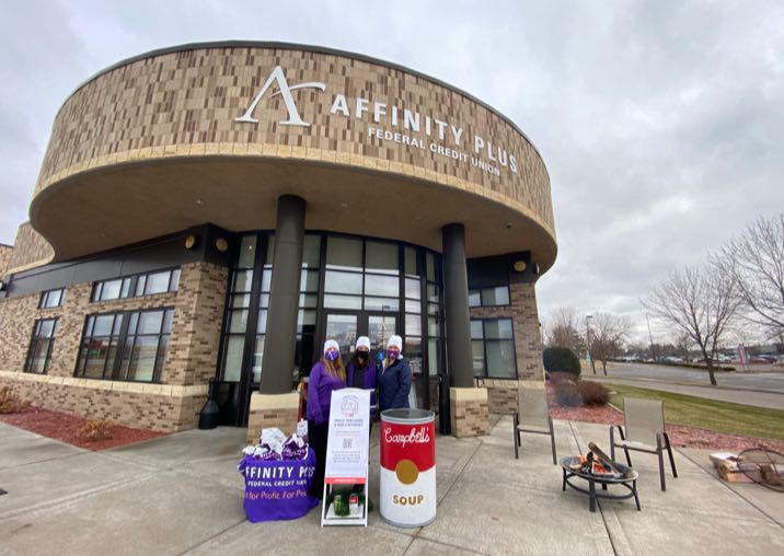Three Affinity Plus employees wearing white beanies and purple shirts, collecting donations in front of an Affinity Plus branch.