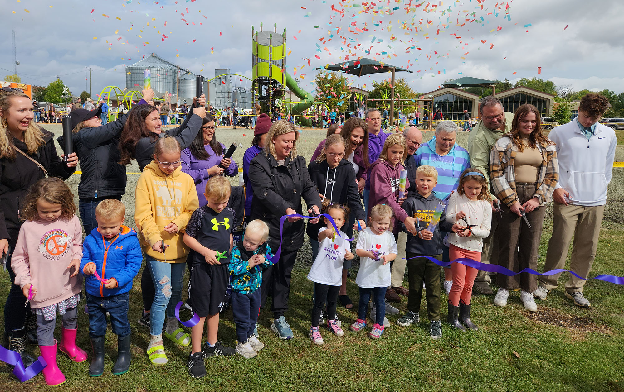 A group of people with confetti and ribbon cutting at a park