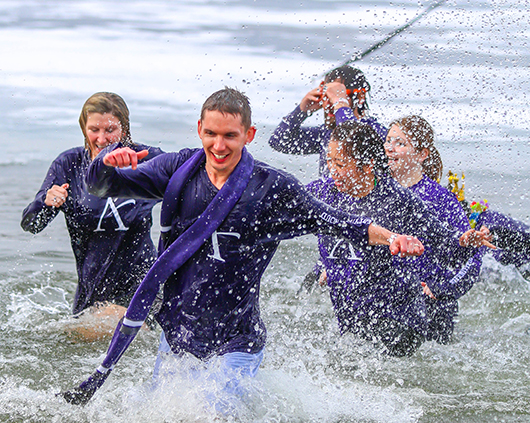 A group with purple shirts splashing in the water