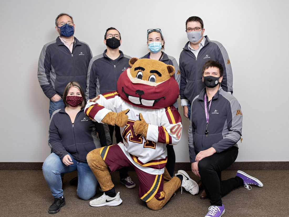 a group of people surrounding Goldy Gopher wearing a mask