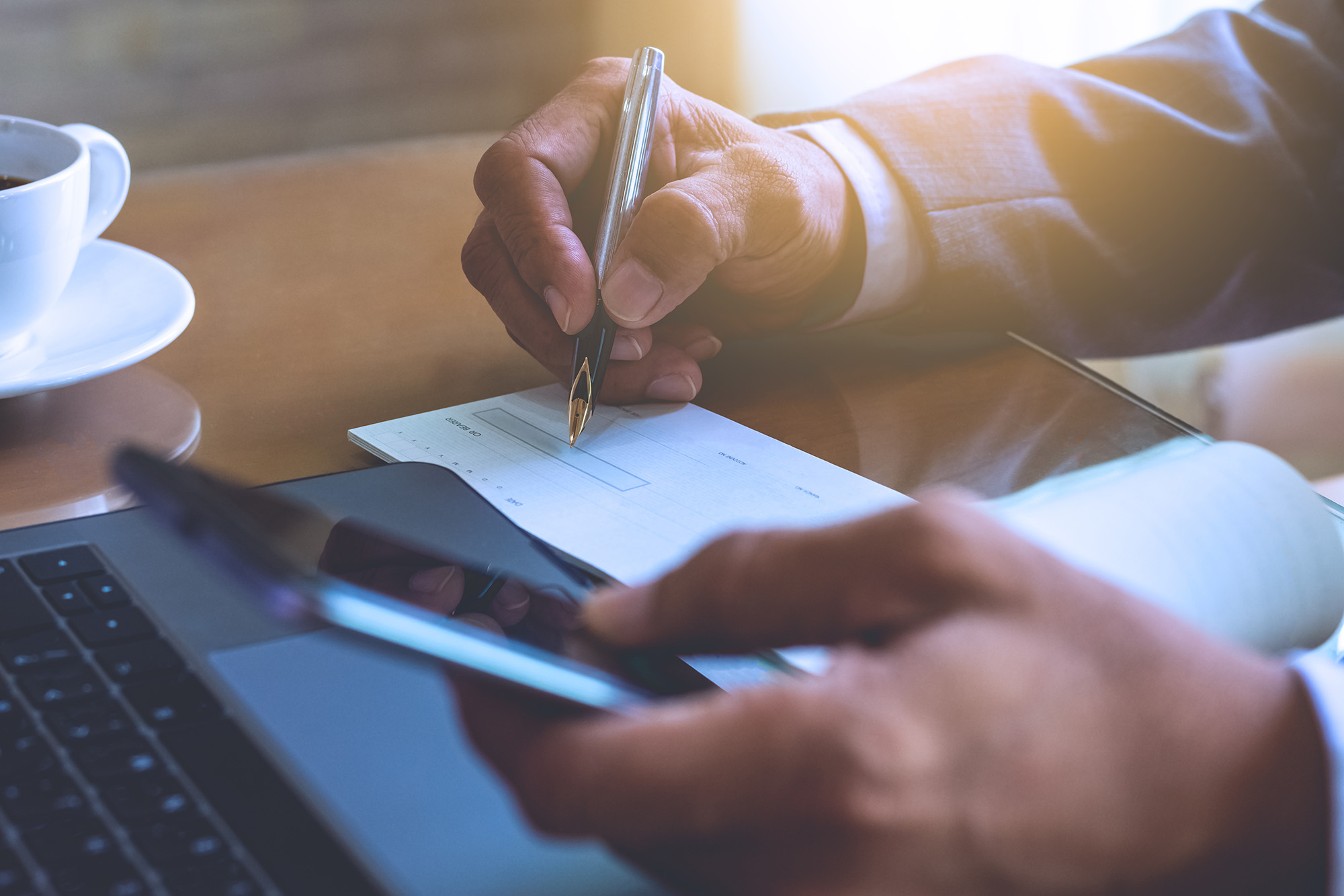 a holding a cell phone signing a check in a check book