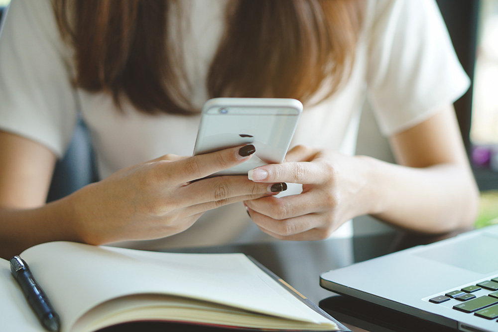 A person looking down at a cell phone with a book open to the left