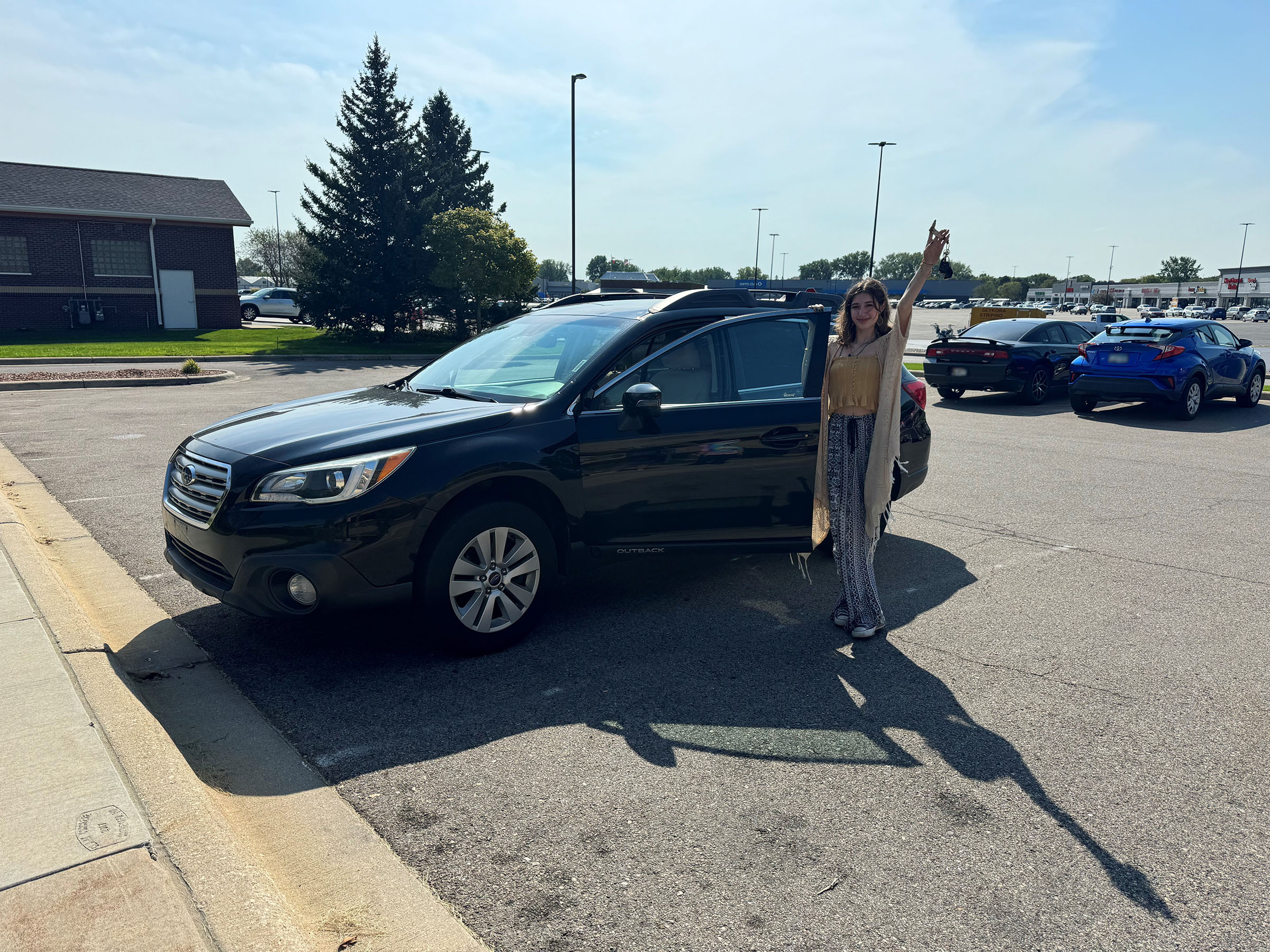 A woman posing in front of a car with a set of keys in hand
