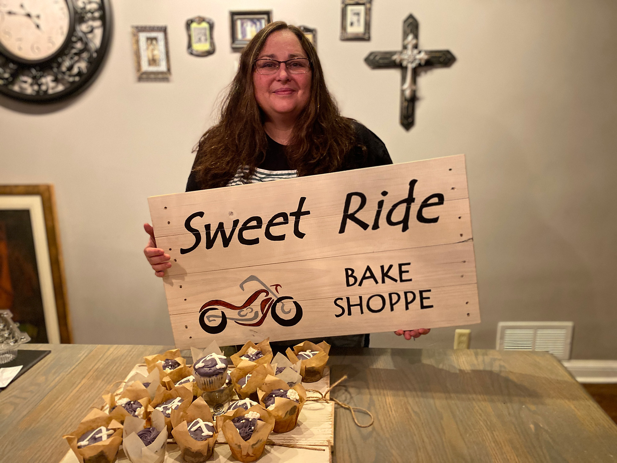 A woman holding up a sign which reads, 'Sweet Ride Bakery Shoppe.'