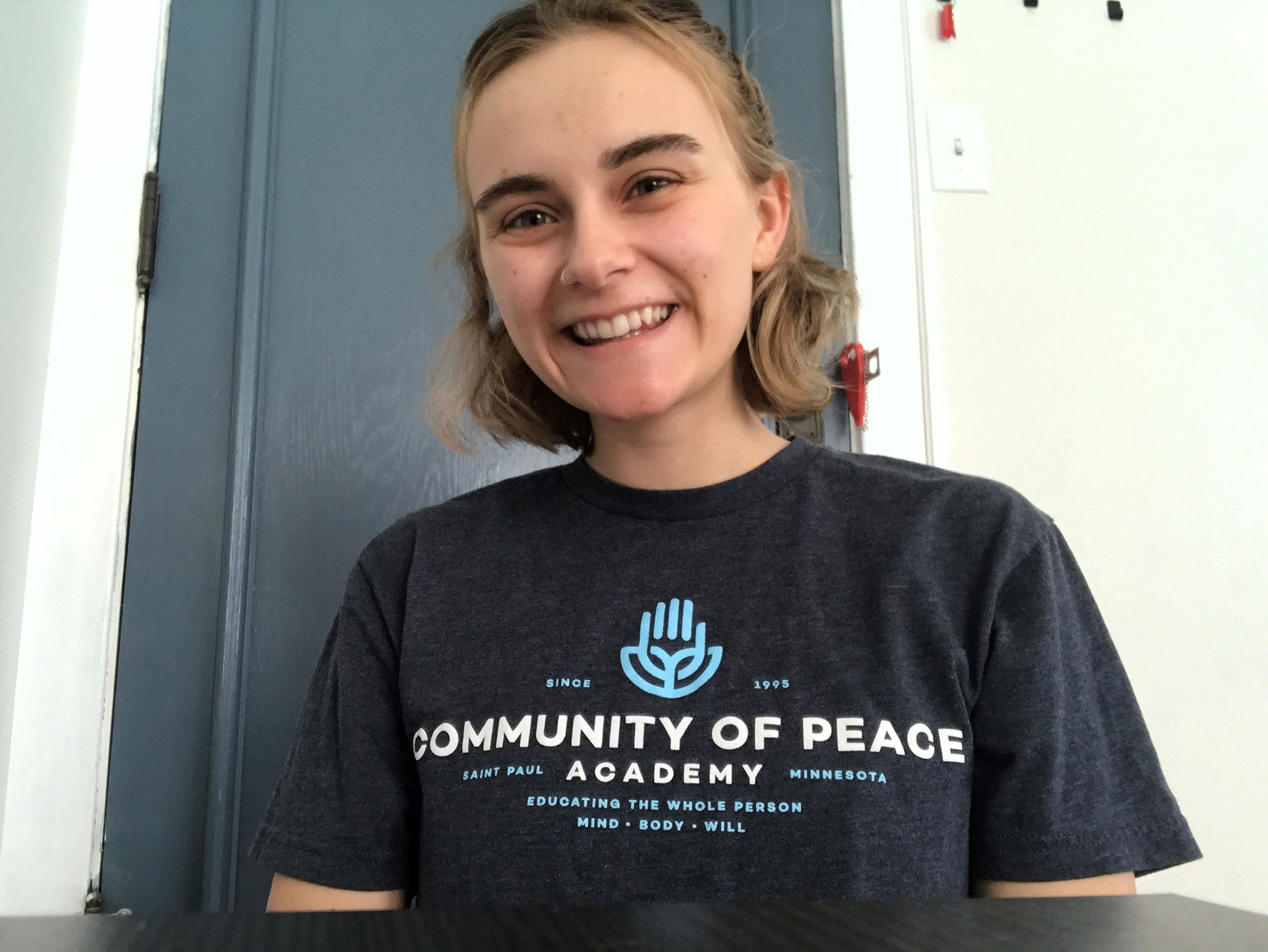 A woman wearing a gray t-shirt that says Community of Peace Academy