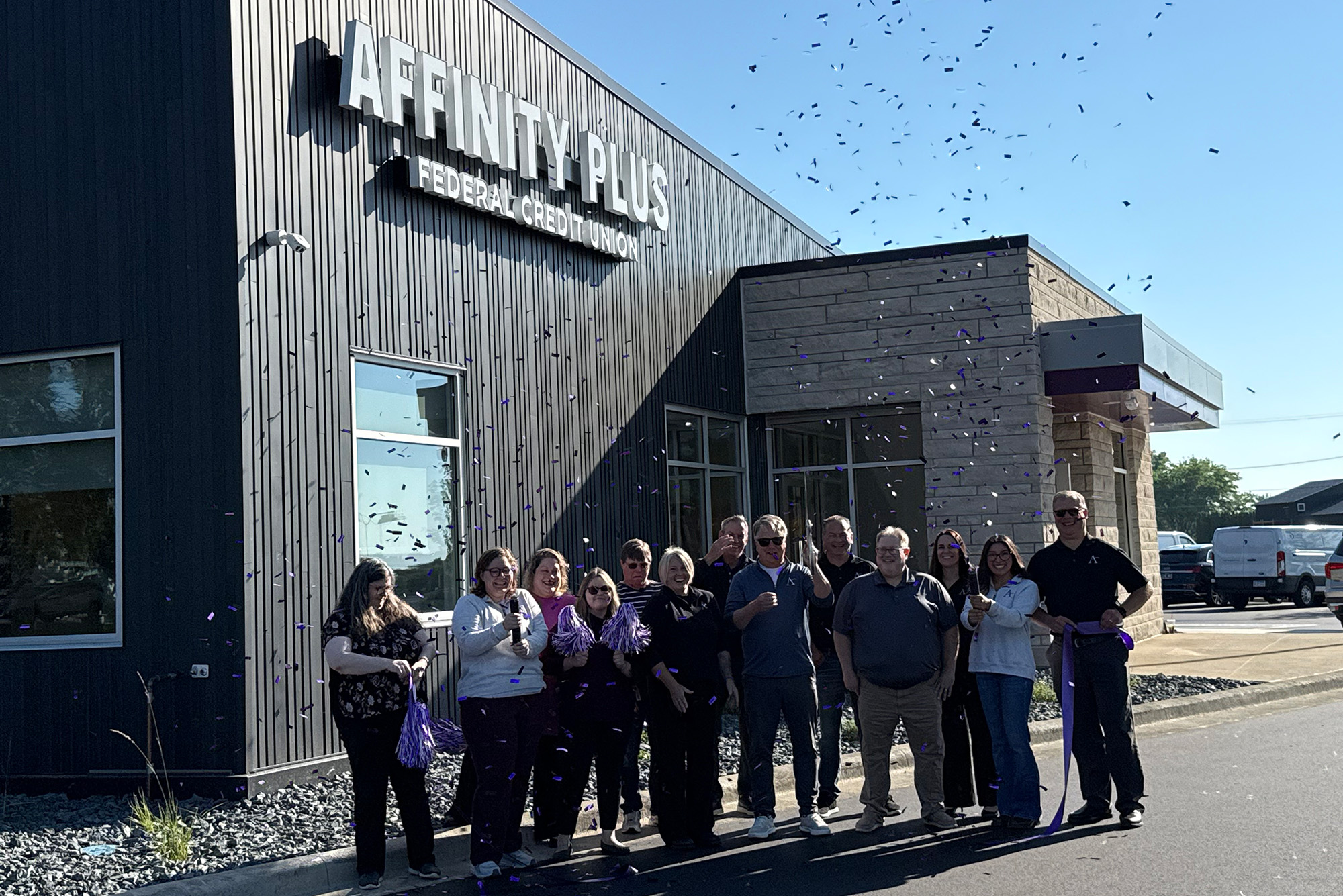 a group of people standing in front of an Affinity Plus branch with confetti