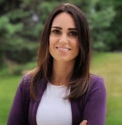 A woman with long brown hair wearing a purple sweater smiling