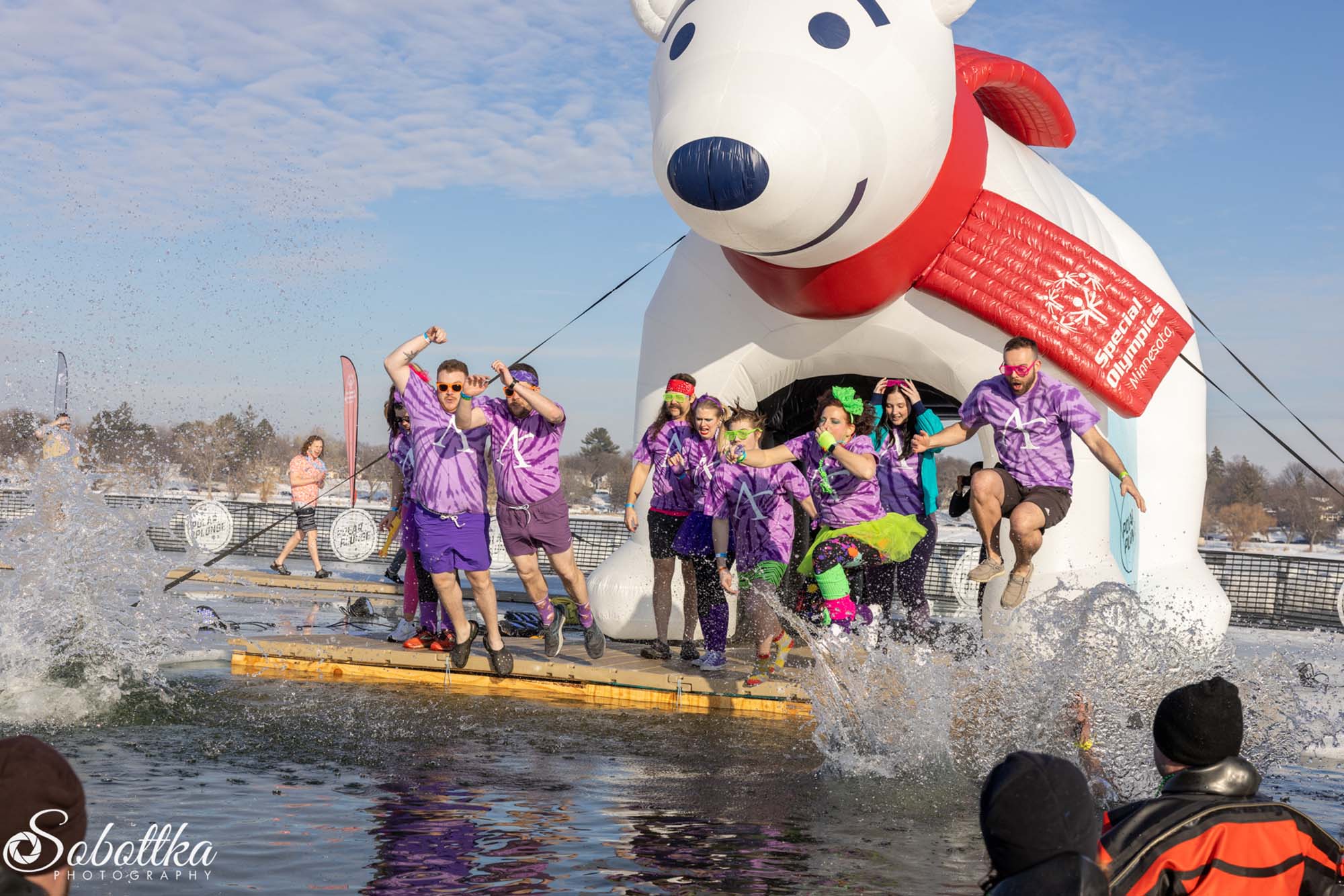 a group of people wearing Affinity Plus shirts jumping into a lake