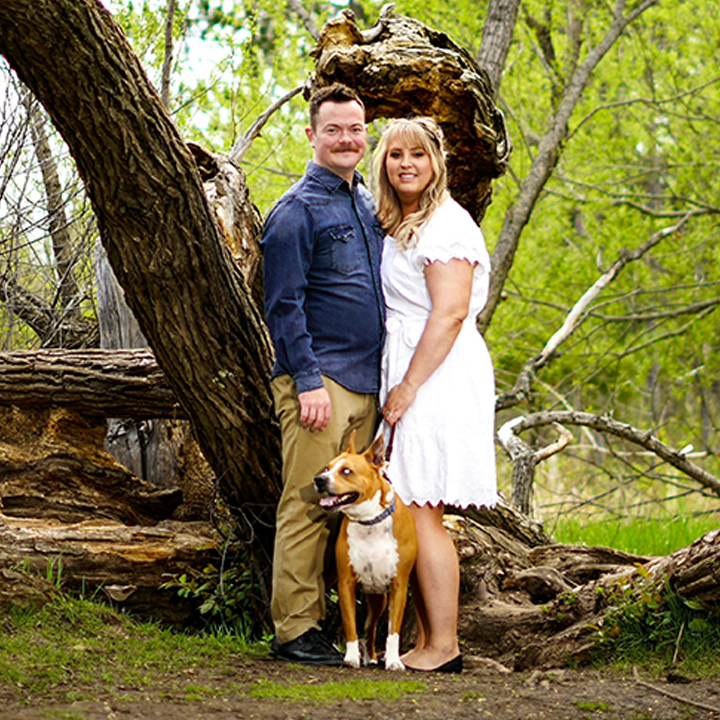 A couple in a wooded area posing with a dog