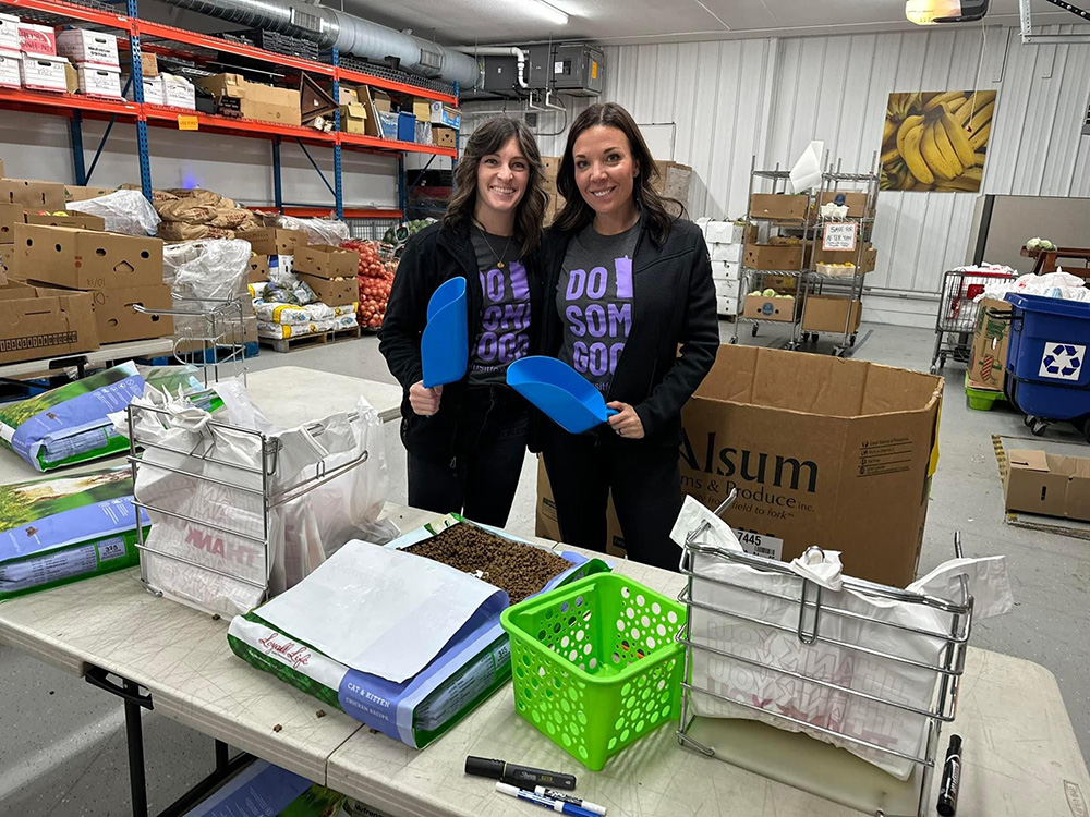 Two women holding blue shovels volunteering on Plus It Forward Day