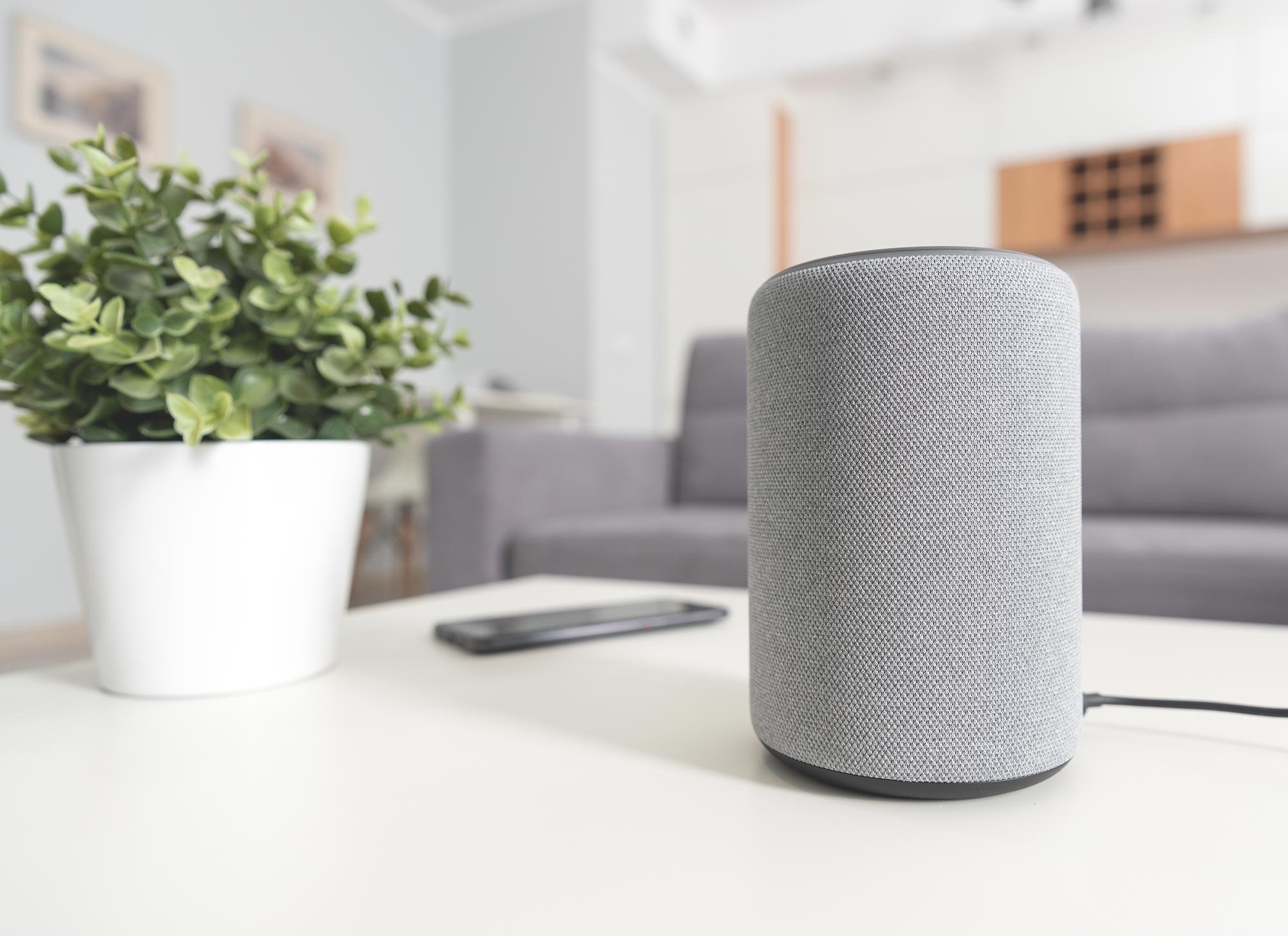 A speaker on a table of a home with a couch blurred in the background