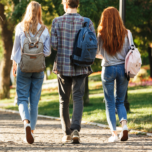 Three students with backpacks walking on a path