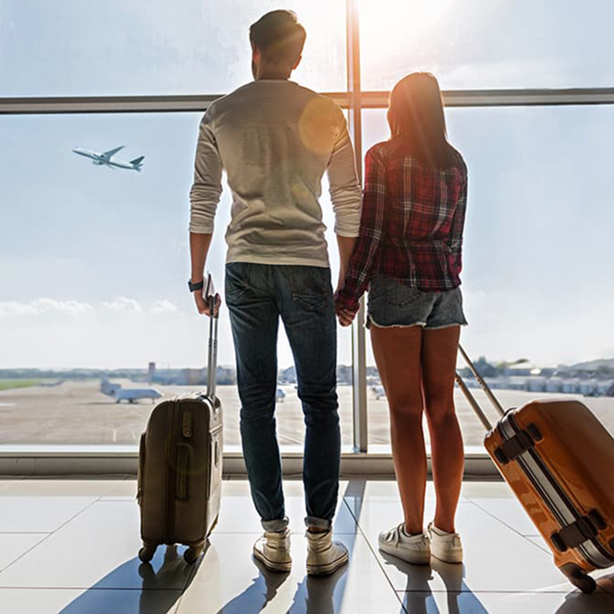 a couple looking out the window at an airplane taking off with suitcases in hand