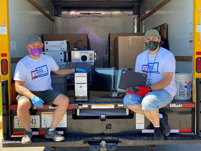 two people sitting on the bed of a trunk surrounded by computer equipment