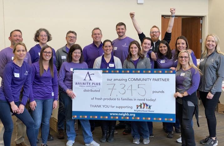 A group of Affinity Plus employees wearing purple and holding a giant check